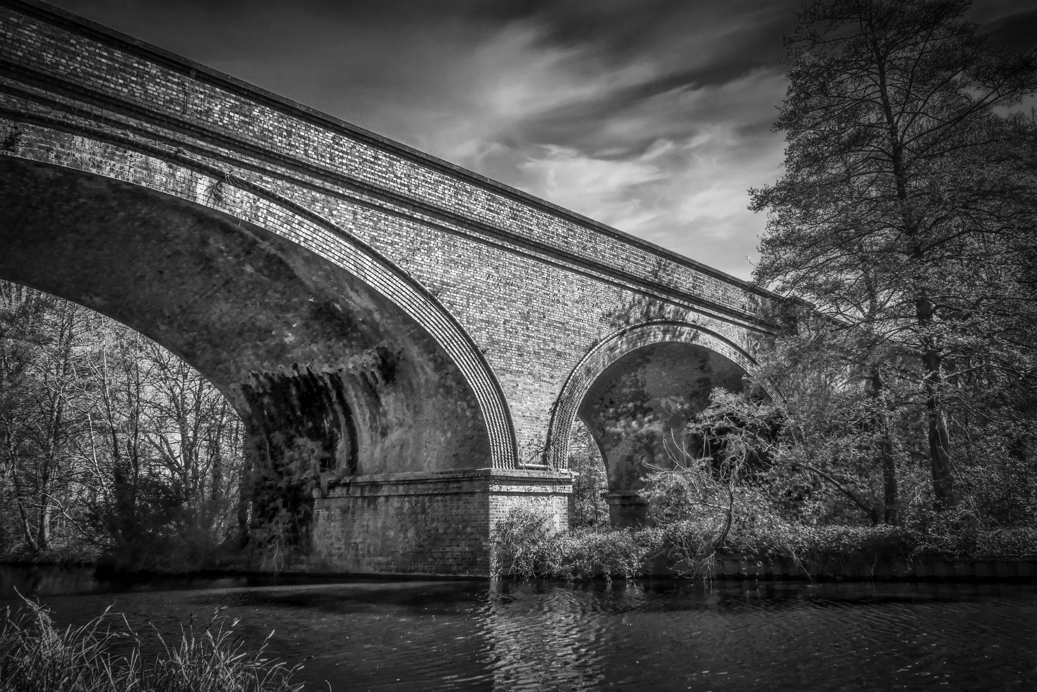 Large brick arch bridge over water in black and white